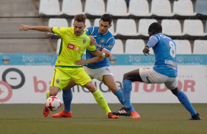 El jugador del Elche Lolo Pla controla el balón ante dos jugadores del Lleida / Santi Iglesias